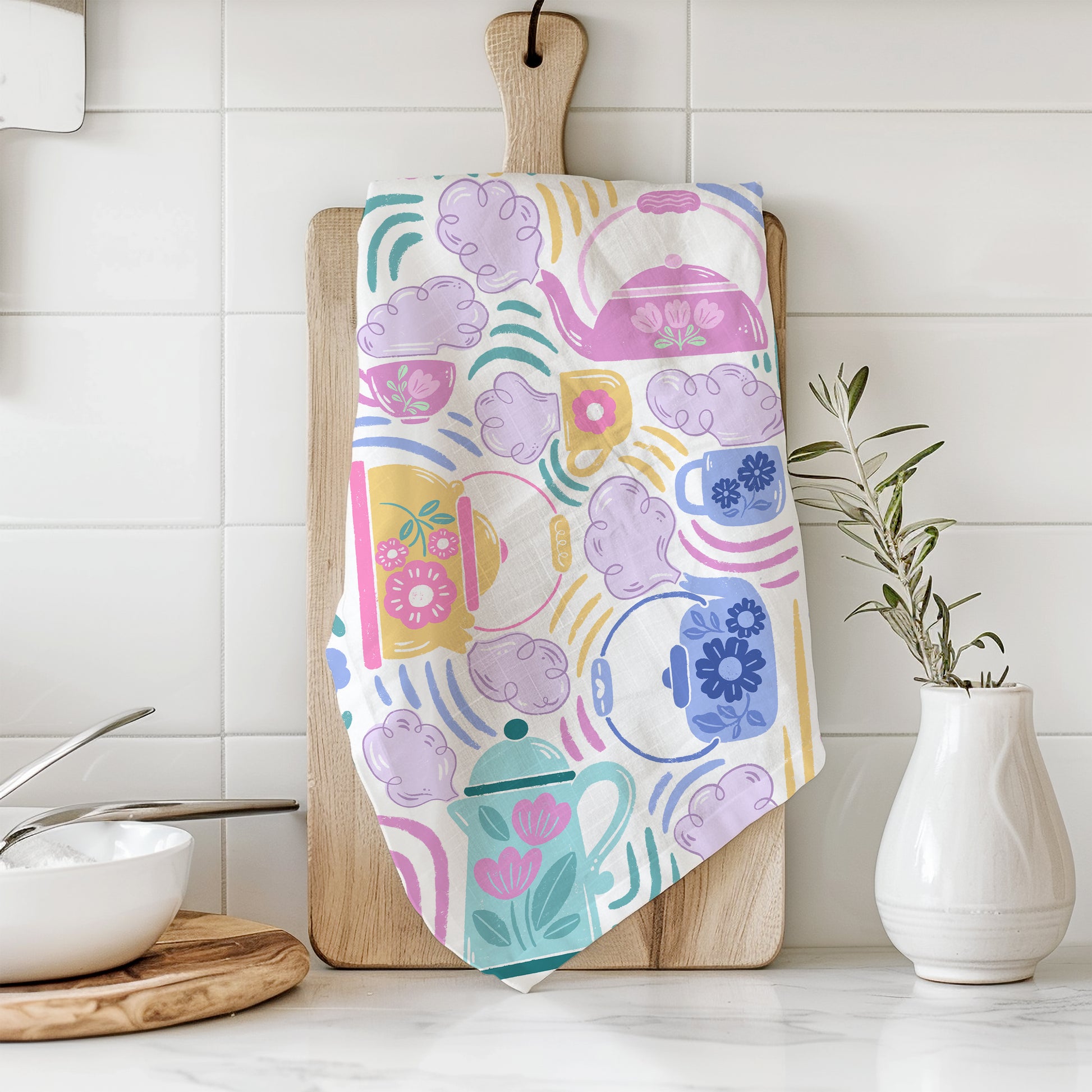 A styled photograph of a white cotton tea towel with a print of teapots and teacups