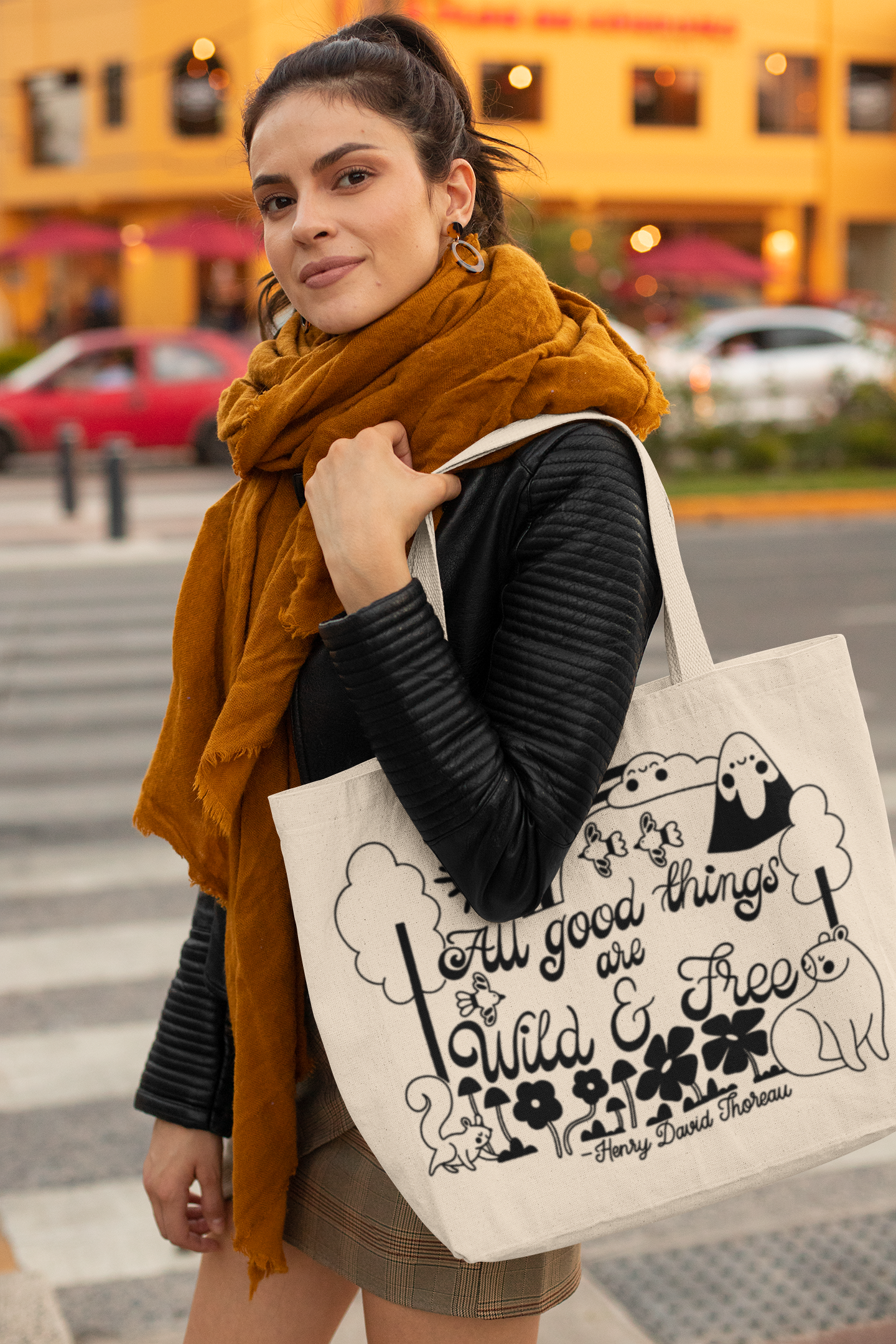 A woman holding a landscape canvas tote bag with black screen-printed scenery artwork